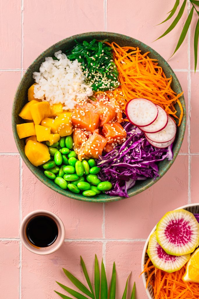 Poke-a bowl with fresh salmon, rice, chuka salad, edamame beans, carrots and red cabbage. Healthy food bowl on pink background. Vertical pour un équilibre et pour perdre du poids